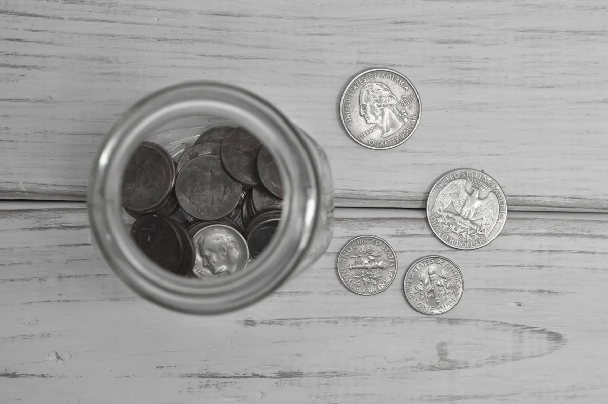 A jar of coins — the cash pound, its colour drained toward grey by the reversed law
